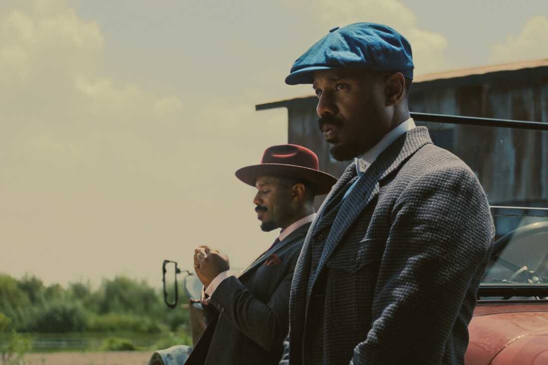 still from Sinners - two different characters, both played by Michael B. Jordan, lean against an old timey car 